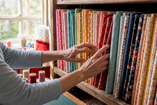 Hands selecting quilting cotton fabric bolts