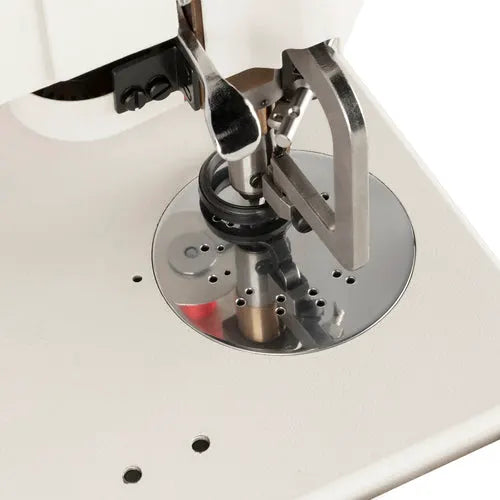 Industrial sewing machine needle area on a white machine with chrome circular throat plate and presser foot.