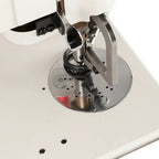 Industrial sewing machine needle area on a white machine with chrome circular throat plate and presser foot.