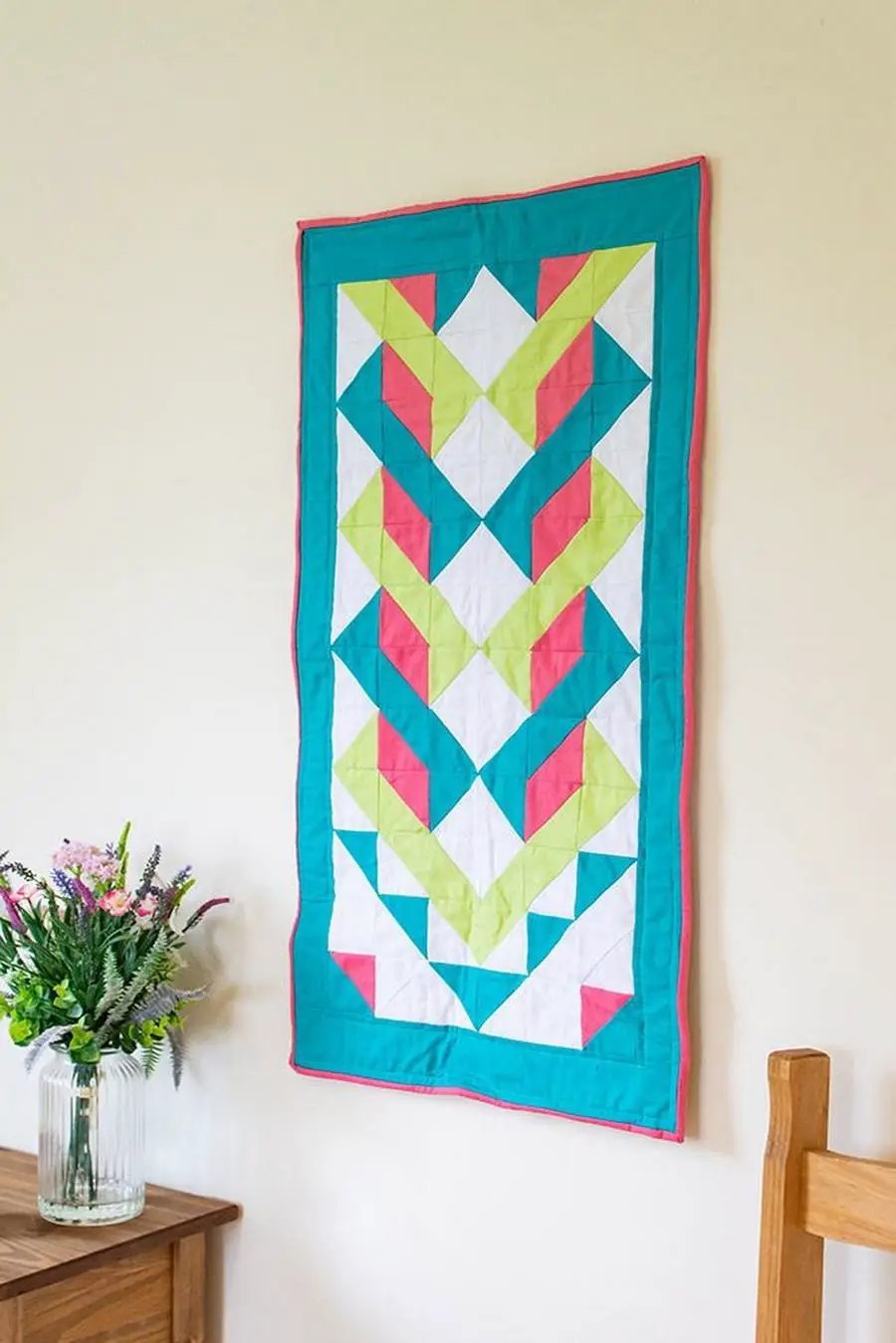 Geometric quilt wall hanging with teal border and bright lime, pink, and white triangles.
