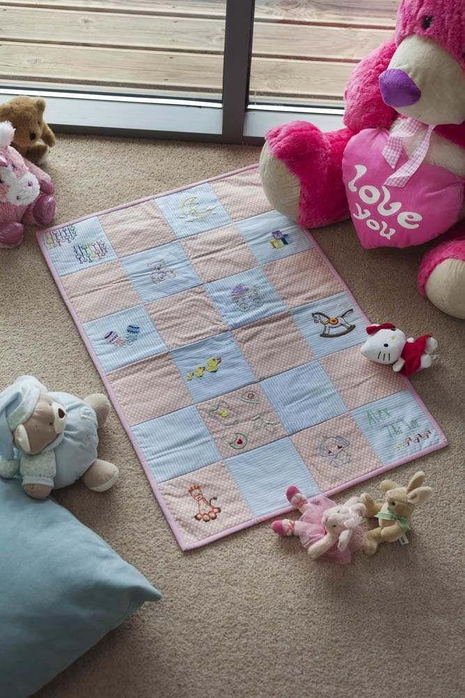 Threaders Embroidery Transfer Sheets; pastel baby quilt with blue and peach squares, surrounded by plush toys.