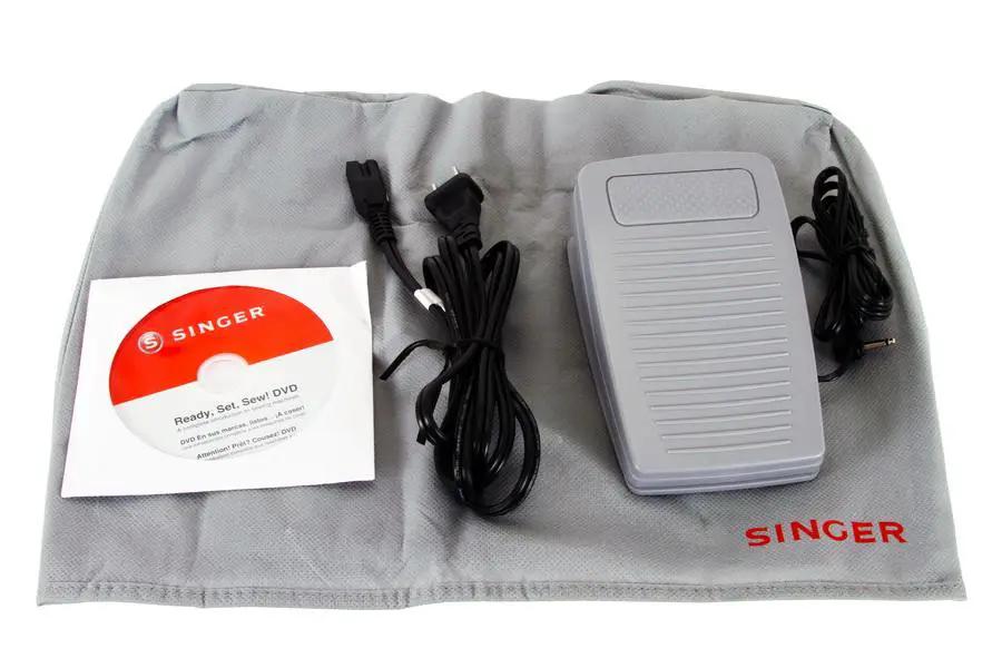 Singer 2010 Superb Computerized Sewing Machine kit; gray foot pedal, cords, and Ready Set Sew DVD on a Singer mat