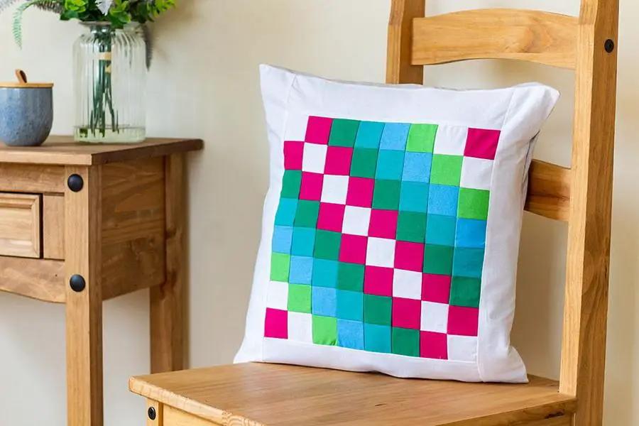 Pillow with a multicolor checkerboard pattern on a white cover, placed on a wooden chair.