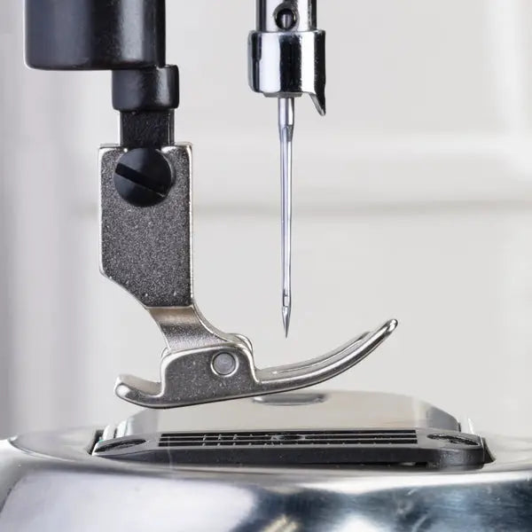 Consew industrial sewing machine needle and presser foot close-up; chrome metal components.