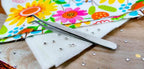 Floriani precision angle tweezers, stainless steel, engraved Floriani, resting on white felt with rhinestones.