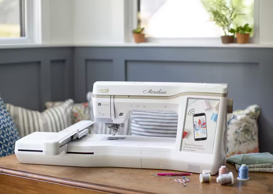 Baby Lock Meridian embroidery machine, white with beige accents, on a wooden table.