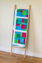 Patchwork quilt on a wooden stand with bright teal, green, blue, and pink blocks.