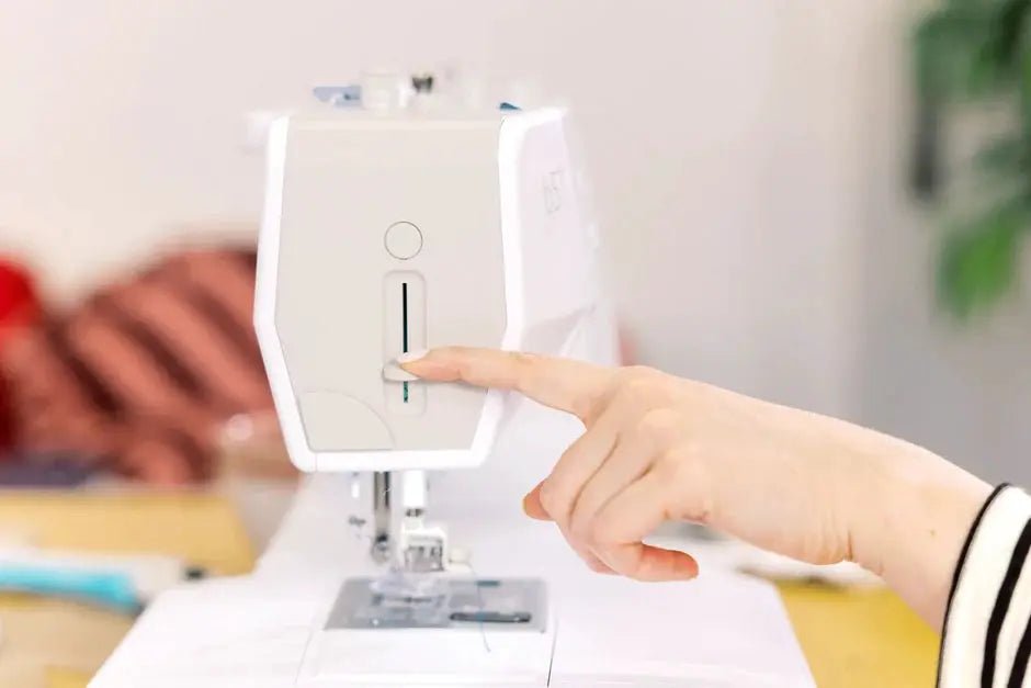Bernette B57 sewing machine by BERNINA, white, with hand on the front panel lever.