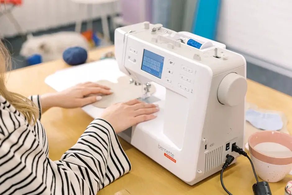 Bernette B57 sewing machine, white, on a wooden table with a person sewing fabric.