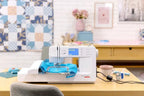 Bernette B59 sewing and embroidery machine, white with blue touchscreen display on a wooden desk.