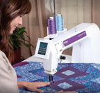 Pfaff Powerquilter 16.0 long-arm quilting machine with white body and purple branding, quilting a blue-purple quilt.