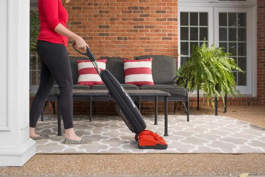 Simplicity S10CV Freedom cordless upright vacuum, red floor nozzle with black wand, cleaning outdoor patio.