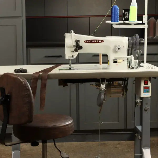 Consew 206RB-5 white walking-foot upholstery sewing machine on a metal table with thread spools