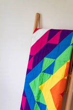 Colorful geometric quilt draped over a wooden easel, featuring bright pink, purple, blue, green and yellow triangles.