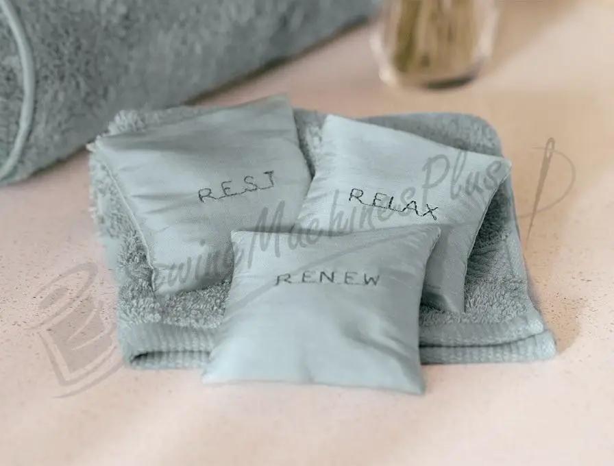 SINGER 8500Q Modern Quilter accessories: three light-blue sachets labeled REST RELAX RENEW on a soft towel