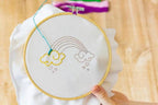Threaders Embroidery Transfer Sheets — Fantasy; rainbow with clouds on white fabric in a wooden hoop