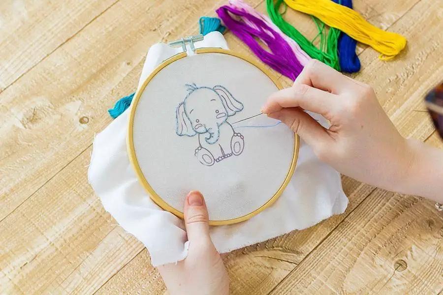 Threaders Embroidery Transfer Sheets - Baby; wooden embroidery hoop displaying a baby elephant sketch with colorful threads.