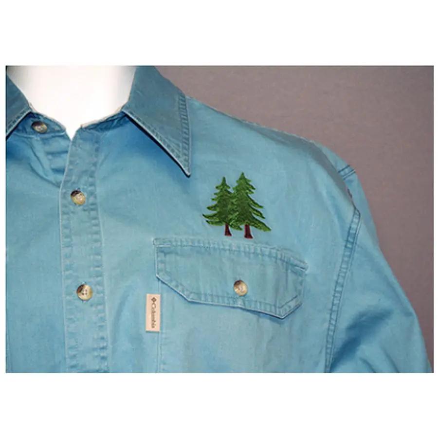 Anita Goodesign Northwoods embroidery design on blue shirt featuring two evergreen trees near chest pocket