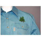 Anita Goodesign Northwoods embroidery design on blue shirt featuring two evergreen trees near chest pocket
