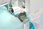 Baby Lock Serenity 4-Thread Serger sewing machine with white body and teal fabric under the presser foot.