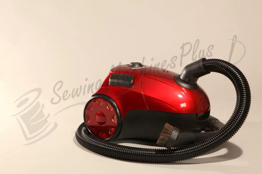 The Bank Robber canister vacuum, red with a black flexible hose and brush attachment.