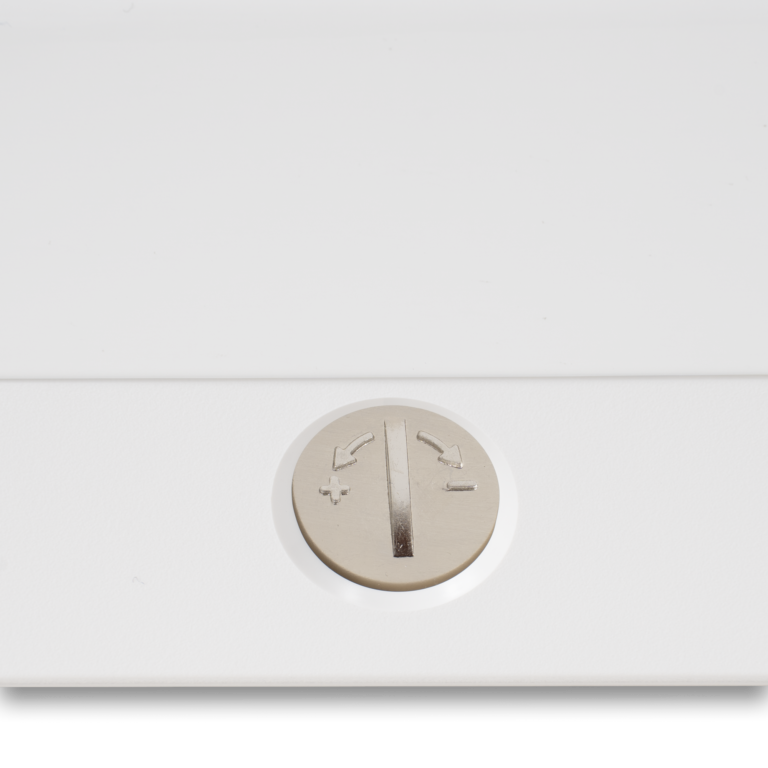 Janome sewing machine control dial on white surface; metallic round knob with arrows and plus/minus