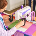Handi Quilter FreeWay Quilt Frame with purple frame and mounted sewing machine, quilter at work.