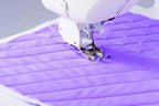 Sewing machine with Juki even feed walking foot stitching a purple quilted fabric