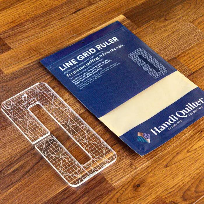 Handi Quilter Line Grid ruler, clear acrylic quilting ruler with white grid, 6x0.5in, shown with blue packaging.