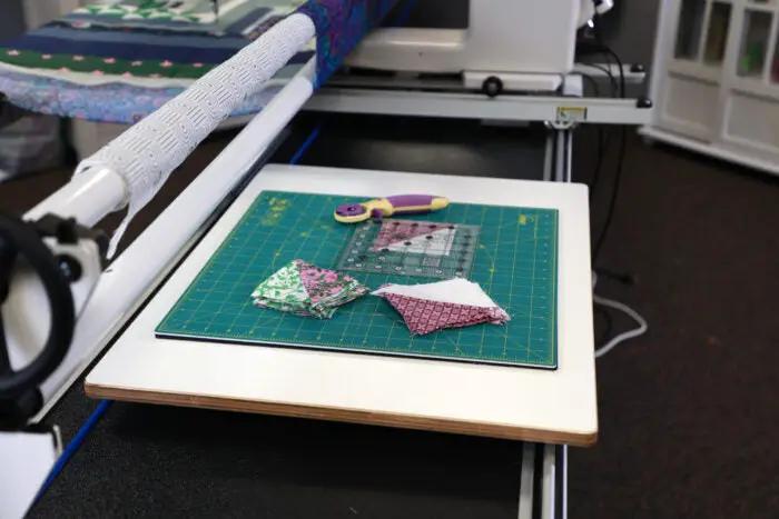 Multi-Use Board Kit by Handi Quilter on a green cutting mat with three fabric scraps and a purple-handled rotary cutter