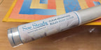 Sew Steady Clear Ruler Work Glider in a silver tube on colorful fabric.