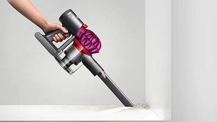 Dyson V7 Motorhead cordless vacuum with gray body and purple cyclone, handheld wand cleaning a shelf edge
