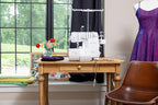 Baby Lock Serenity 4-Thread Serger sewing machine, white, on a wooden table beside a dress form.