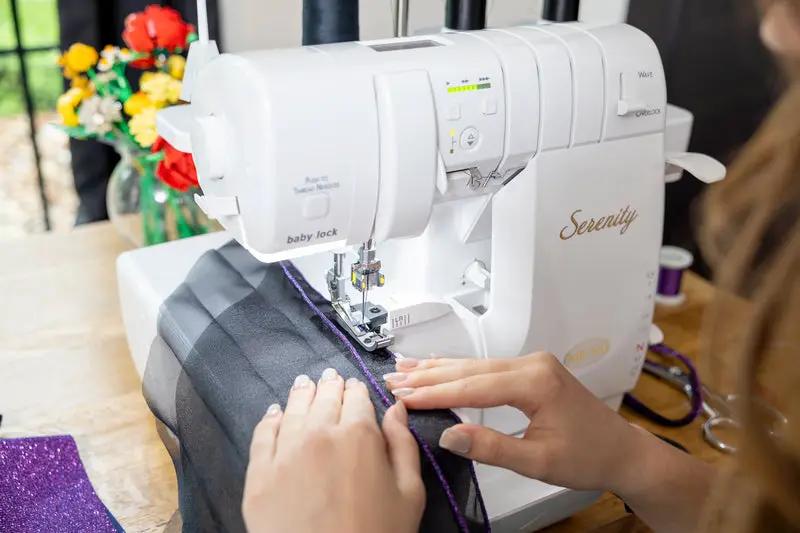 Baby Lock Serenity 4-Thread Serger sewing machine in white with hands guiding purple fabric.