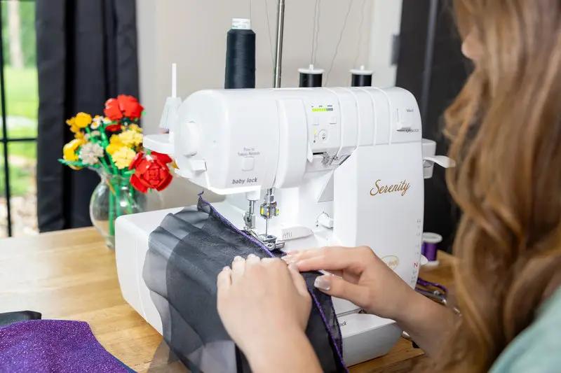 Baby Lock Serenity 4-Thread Serger in white, serging purple fabric on a wooden table.