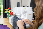Baby Lock Serenity 4-Thread Serger in white, serging purple fabric on a wooden table.
