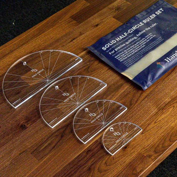 Handi Quilter Solid Half-Circle Ruler Set, 5 clear acrylic rulers on a wood table with blue packaging