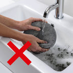 Dyson vacuum demo: hands rinse a round dark gray pad under running water in a white sink with red Xs