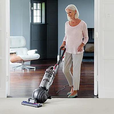 Dyson Cinetic Big Ball Animal + Allergy UP14ANA vacuum in gray with a transparent canister, in use by a woman.