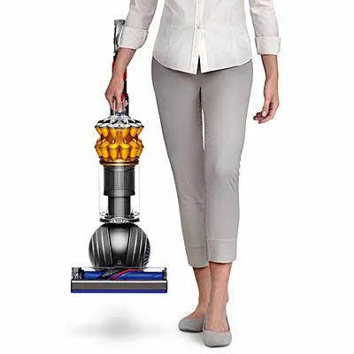 Dyson Small Ball Multifloor UP15MF vacuum held by person; upright canister with orange cyclone and blue base.