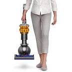 Dyson Small Ball Multifloor UP15MF vacuum held by person; upright canister with orange cyclone and blue base.