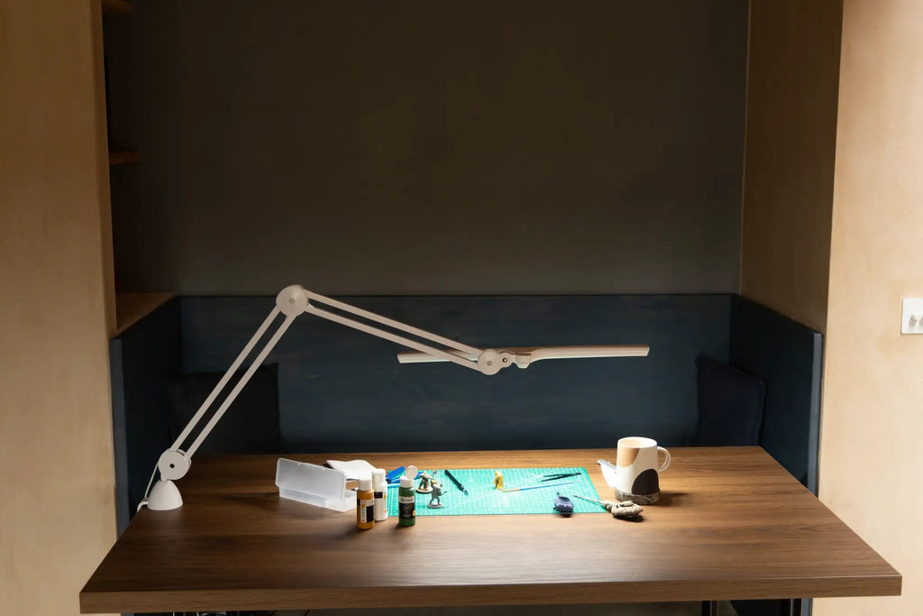Daylight Lumi LED Task Lamp on a wooden desk, white metal with adjustable arms