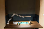 Daylight Lumi LED Task Lamp on a wooden desk, white metal with adjustable arms