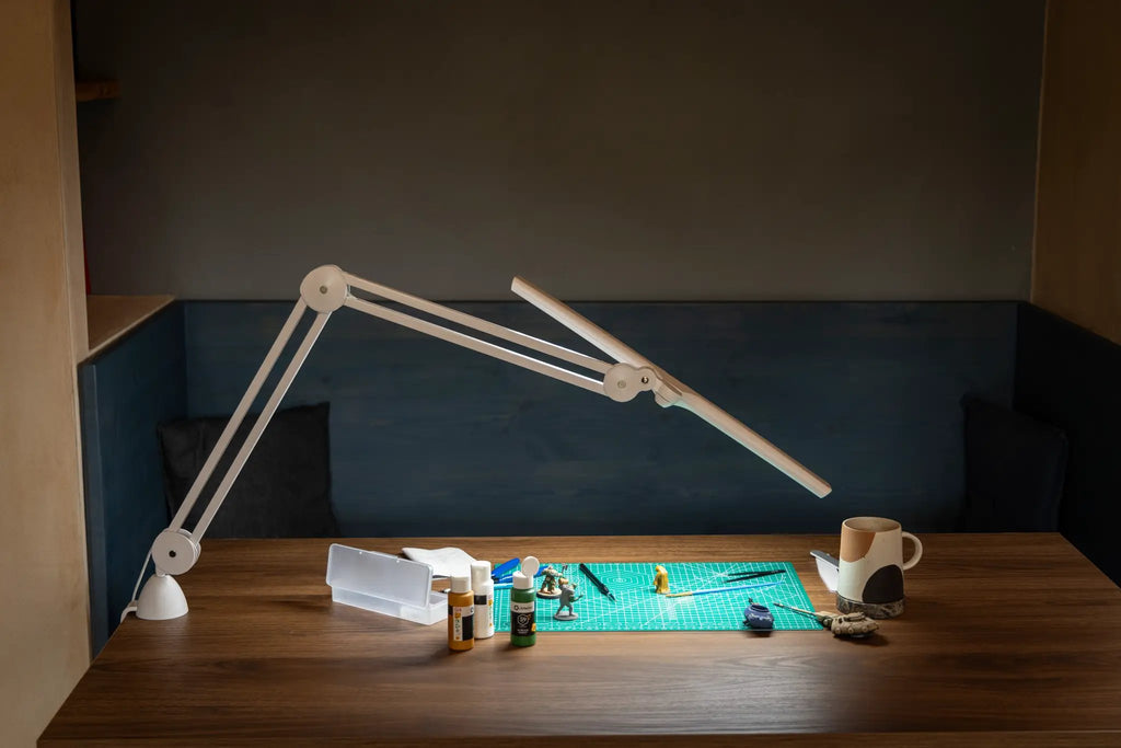 Daylight Lumi LED Task Lamp, white adjustable desk lamp on a wood desk with crafting supplies.