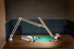 Daylight Lumi LED Task Lamp on a wooden desk with craft supplies, paints, and a mug