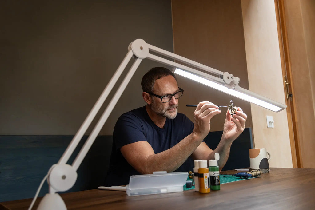 Daylight Lumi LED Task Lamp, white adjustable desk light over a crafts table.