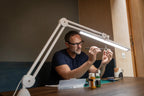Daylight Lumi LED Task Lamp, white adjustable desk light over a crafts table.