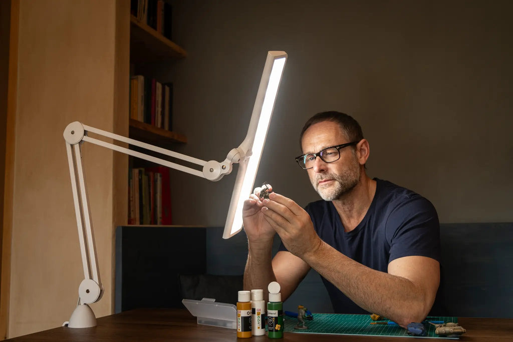 Daylight Lumi LED Task Lamp, white adjustable desk lamp on a workbench.