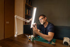 Daylight Lumi LED Task Lamp, white adjustable arm, bright panel; man painting miniatures at desk.