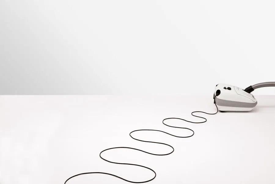 SEBO AIRBELT E3 Premium canister vacuum in Arctic White with grey accents, cord trailing on white surface.